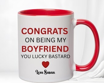 Puede incluir: Taza de cerámica blanca con interior y asa rojos. La taza presenta el texto "CONGRATS ON BEING MY BOYFRIEND YOU LUCKY BASTARD" en rojo, con un corazón rojo y la firma "Love Susan".