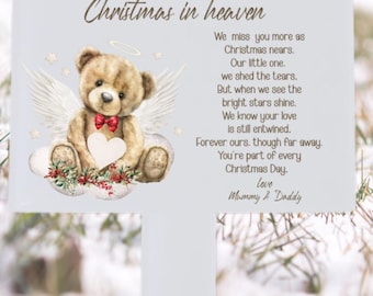 Puede incluir: Un letrero blanco con el texto "Christmas in heaven" y un poema. Presenta un oso de peluche con alas de ángel, una pajarita roja y un corazón. Un conmovedor homenaje.
