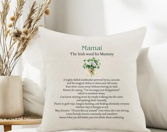 Puede incluir: Cojín blanco con el texto "Mamaí, la palabra irlandesa para mamá" en verde. El cojín presenta una ilustración floral y una descripción humorística de las habilidades y rasgos de una madre.