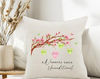 Puede incluir: Un cojín cuadrado blanco con un diseño de acuarela de una rama de árbol con flores rosas y mariposas verdes. El cojín tiene tres etiquetas con forma de corazón y el texto "A Nannie's Love is Unconditional."