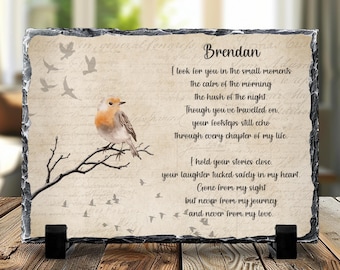 Puede incluir: Placa rectangular de pizarra con borde decorativo. Presenta una ilustración en acuarela de un petirrojo posado en una rama, con pájaros volando y un poema dedicado a "Brendan". La placa está soportada por dos soportes negros.