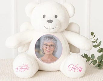 Puede incluir: Un oso de peluche blanco con alas de ángel, con una foto de una mujer en un círculo rosa. Las palabras "My Angel" y "Mum" están impresas en rosa en las patas. Un conmovedor recuerdo.