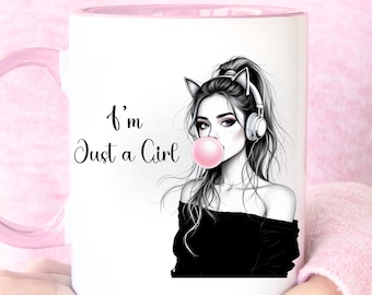Puede incluir: Taza de cerámica blanca con interior y asa rosas. La taza presenta una ilustración en blanco y negro de una chica con orejas de gato, auriculares y una burbuja de chicle. El texto "I'm Just a Girl" también está en la taza.