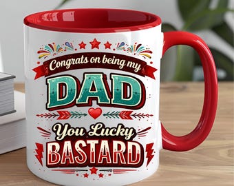 Puede incluir: Taza de cerámica blanca con interior y asa rojos. La taza presenta el texto "Congrats on being my DAD, You Lucky BASTARD" en un diseño turquesa y rojo con elementos decorativos. La taza está sobre una superficie de madera.