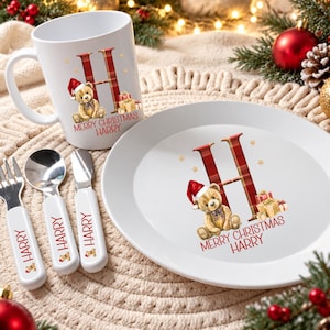 Puede incluir: Una taza blanca, un plato blanco, un tenedor, una cuchara y un cuchillo. Cada pieza presenta una letra H en cuadros rojos, un oso de peluche con gorro de Pap&aacute; Noel, regalos y el texto rojo Merry Christmas Harry impreso.