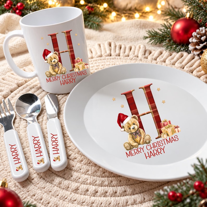 Puede incluir: Una taza blanca, un plato blanco, un tenedor, una cuchara y un cuchillo. Cada pieza presenta una letra H en cuadros rojos, un oso de peluche con gorro de Pap&aacute; Noel, regalos y el texto rojo Merry Christmas Harry impreso.