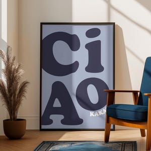 Könnte beinhalten: Gerahmtes Poster mit dem Wort "CIAO" in großen, dunkelblauen Buchstaben auf hellblauem Hintergrund. Das Wort "KAKA" ist in kleinen, weißen Buchstaben unter "AO" gedruckt. Das Poster wird in einem Raum mit einem blauen Sessel und einem gemusterten Teppich ausgestellt.