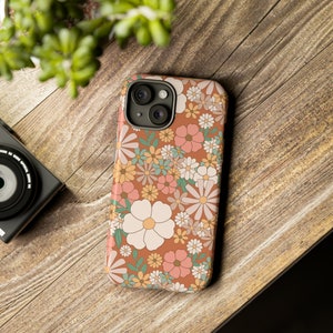 May include: A phone case with a floral pattern. The case is brown with white, pink, and green flowers. The case has a camera cutout on the back.