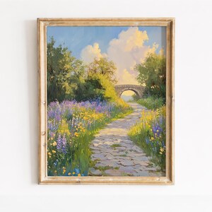 May include: Framed landscape painting featuring a stone path leading to a bridge under a blue sky with fluffy clouds. The path is lined with purple and yellow wildflowers, and lush green trees frame the scene. The painting is in a gold-colored frame.