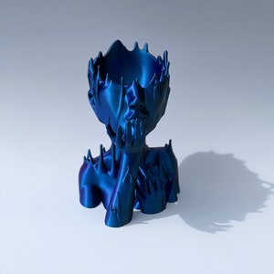 Könnte beinhalten: Eine blaue, abstrakte, 3D-gedruckte Skulptur einer Person mit einer Vase auf dem Kopf. Die Skulptur hat eine glatte, metallische Oberfläche.