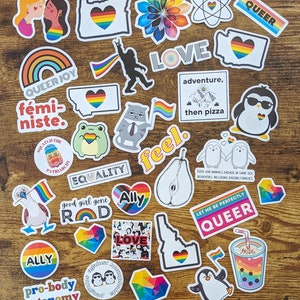May include: A collection of colorful stickers with rainbow designs and messages of love, equality, and acceptance. The stickers feature phrases like "Queer Joy", "Ally", "Pro-body Autonomy", "Good Girl Gone Rad", "Feel", "Love", "Adventure, then Pizza", "Let Me Be Perfectly Queer", and "Equality".