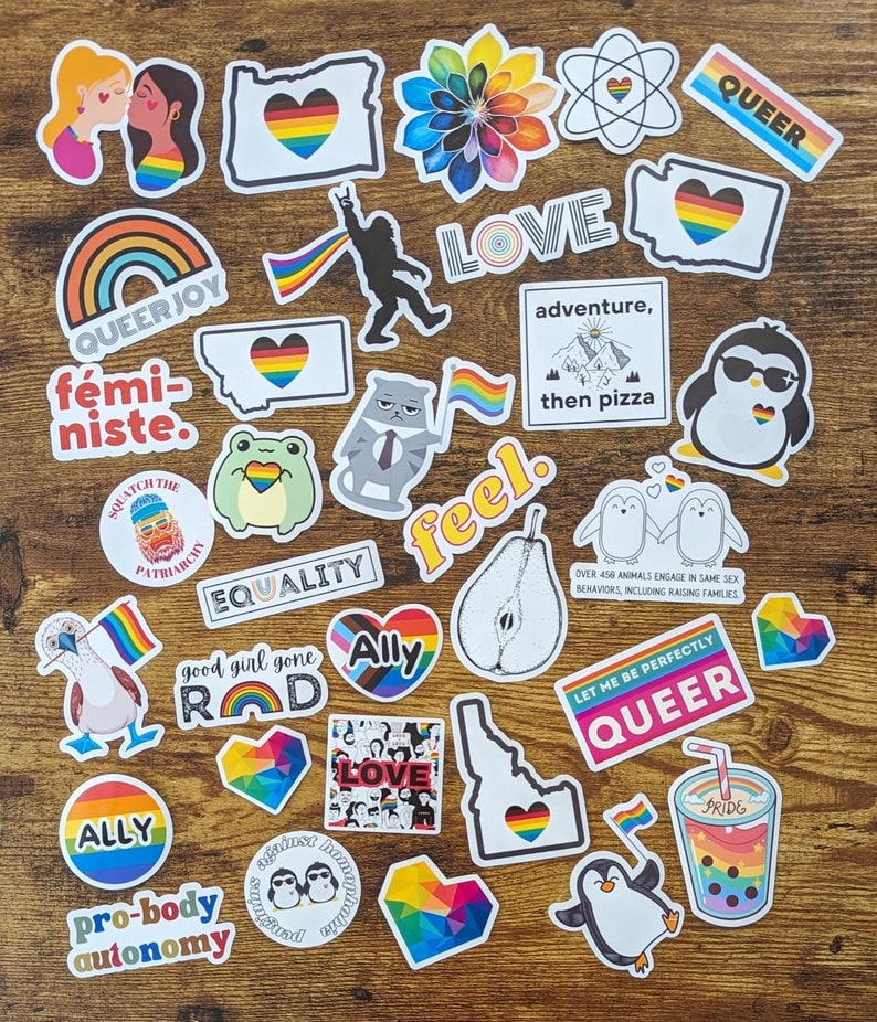 May include: A collection of colorful stickers with rainbow designs and messages of love, equality, and acceptance. The stickers feature phrases like "Queer Joy", "Ally", "Pro-body Autonomy", "Good Girl Gone Rad", "Feel", "Love", "Adventure, then Pizza", "Let Me Be Perfectly Queer", and "Equality".