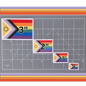 May include: Four different sizes of a pride flag sticker with a black, brown, light blue, pink, white, yellow, green, and blue color scheme. The stickers are 3 inches, 2 inches, 1.5 inches, and 1 inch in size.