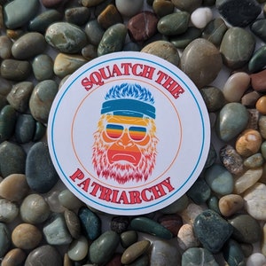 K&ouml;nnte beinhalten: Ein runder Aufkleber mit wei&szlig;em Hintergrund und einem Farbschema in Rot, Orange, Gelb und Blau. Der Aufkleber zeigt eine Cartoon-Illustration eines Sasquatch, der eine Sonnenbrille und ein Stirnband tr&auml;gt. Der Text "Squatch the Patriarchy" ist in einem Kreisbogen um den Sasquatch geschrieben.