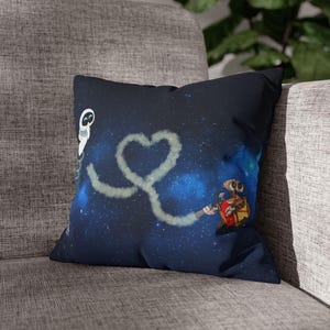 Op de afbeelding: Een vierkant kussen met een ruimtethema. Het kussen toont een donkerblauwe achtergrond met een hartvormig dampsporen. Het ontwerp bevat stripfiguren en een sterrenhemel, wat een grillige esthetiek creëert.