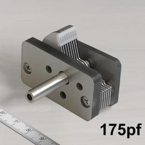 Puede incluir: Un condensador variable de color plateado con un eje de metal y una perilla de plástico blanco. El condensador tiene una capacidad de 175pF.