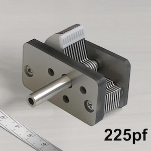 Puede incluir: Un condensador variable de metal plateado con una perilla de plástico blanco. El condensador tiene una capacidad de 225pf.