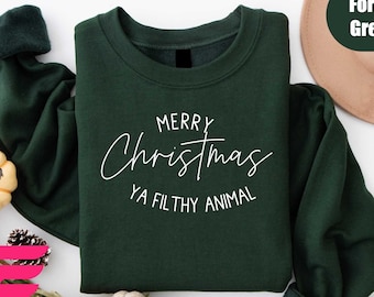 May include: Forest green sweatshirt with the text "MERRY Christmas YA FILTHY ANIMAL" in white script. The sweatshirt is displayed with a tan hat and decorative pumpkins.