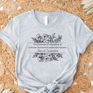 May include: Gray t-shirt with a black floral design and the text "The purpose of education is to know God and to make Him known. Classical Conversations."
