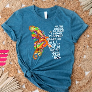 May include: Teal blue t-shirt with an orange ribbon and a colorful butterfly graphic. The text on the shirt reads "Multiple Sclerosis is a journey I never planned or asked for but I choose to love life hate the disease and fight."