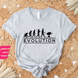 May include: A gray t-shirt with a black graphic of the evolution of man, ending with a skier. The text "EVOLUTION" is printed below the graphic.