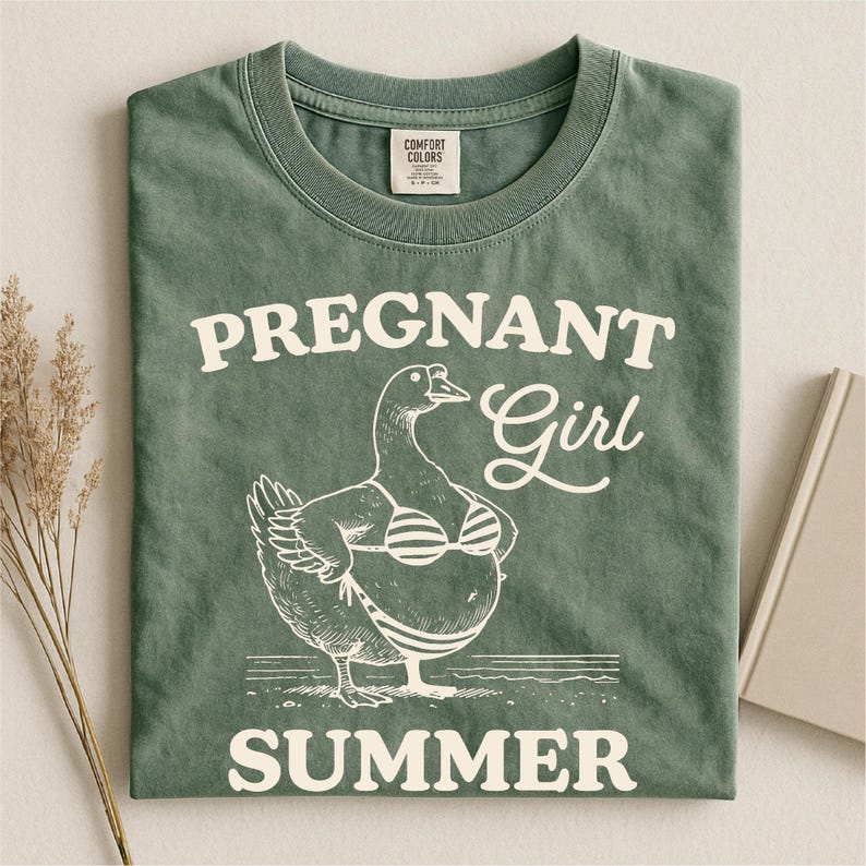 A green t-shirt with a graphic design depicting a duck wearing a bikini top and the text "Pregnant Girl Summer" printed on it.