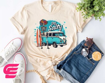 May include: A beige t-shirt with a graphic of a skeleton holding a surfboard and standing next to a blue and white vintage van. The graphic also includes the text "Stay Salty".