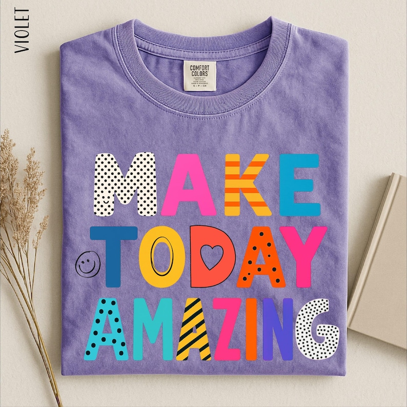 A purple t-shirt with the text "MAKE TODAY AMAZING" printed on it, along with various colorful and playful lettering designs.