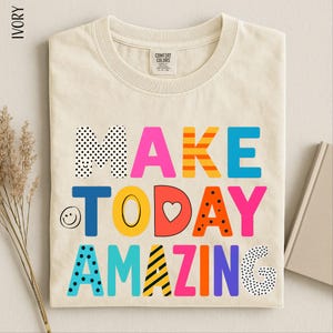 A beige t-shirt with a colorful text design that says "MAKE TODAY AMAZING" printed on it.