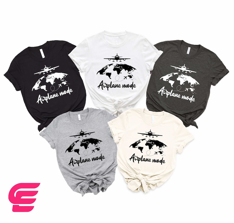 May include: Five short-sleeve t-shirts in various colors, including black, white, gray, and beige, feature a graphic design of a plane flying over a world map. The text 'Airplane mode' is printed below the graphic on each shirt. The shirts are arranged on a white background.  The design is simple and stylish, suitable for travel enthusiasts.