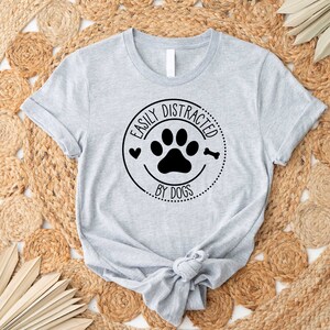 May include: A grey t-shirt with a black paw print and the text "Easily Distracted by Dogs" in a circle.