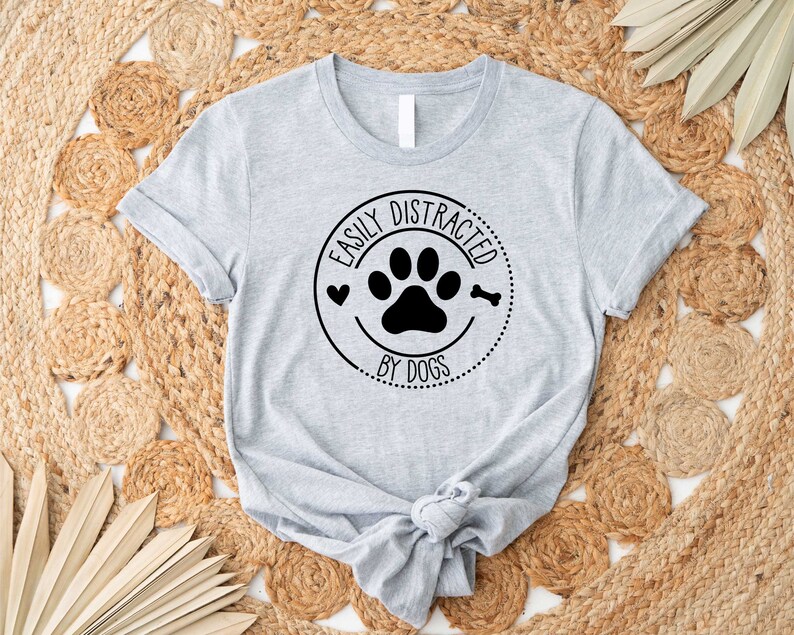 May include: A grey t-shirt with a black paw print and the text "Easily Distracted by Dogs" in a circle.