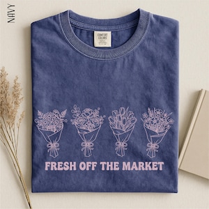 A navy blue t-shirt with a graphic design of four bouquets of flowers and the text "FRESH OFF THE MARKET" printed on it.