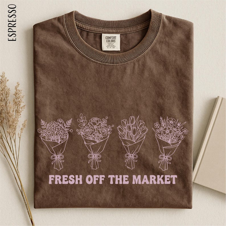 a brown t-shirt with a graphic design of four bouquets of flowers, each with a bow, and the text "FRESH OFF THE MARKET" printed on it.