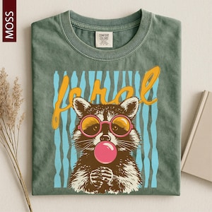 A green t-shirt with a graphic design featuring a raccoon wearing pink bubble gum and sunglasses, along with the word "Frol" written above the raccoon.