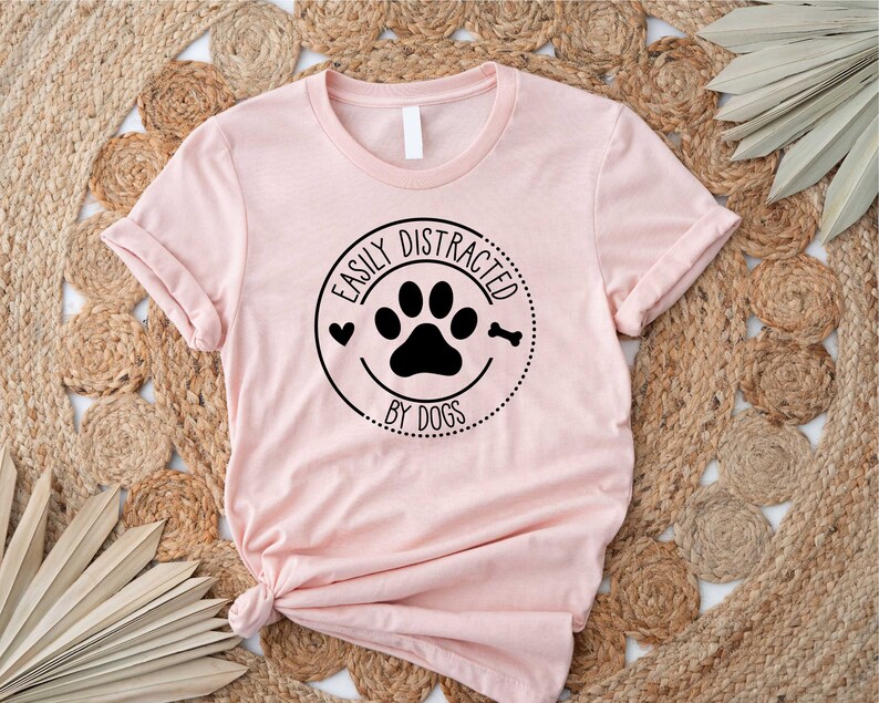 May include: A pink t-shirt with a black circle graphic that says "Easily Distracted by Dogs" with a paw print and a bone inside the circle.