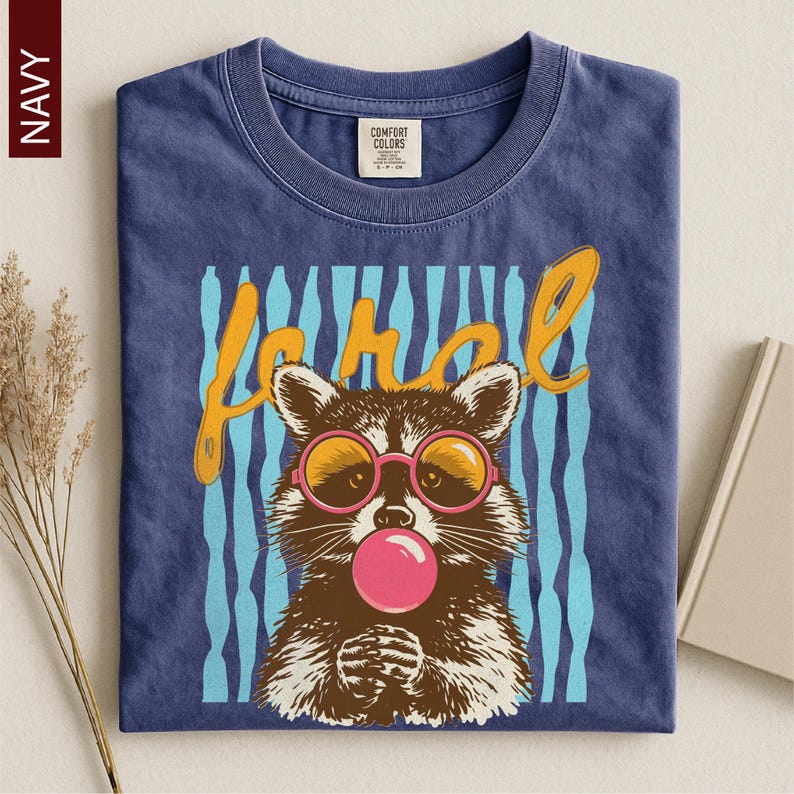 A navy blue t-shirt with a graphic design of a raccoon wearing pink bubble gum and sunglasses, along with the word "Raccoon" written above it.
