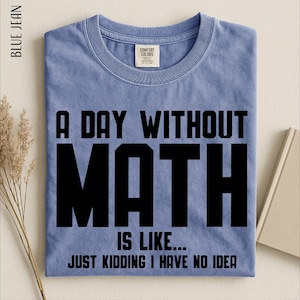 May include: A blue short-sleeved t-shirt with a crew neckline. The shirt features black text that reads A DAY WITHOUT MATH IS LIKE... JUST KIDDING I HAVE NO IDEA. The garment has a Comfort Colors brand label on the inside of the collar.