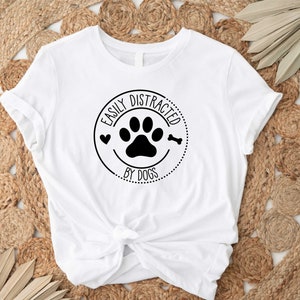 May include: White t-shirt with a black circle graphic that says "Easily Distracted by Dogs" with a paw print and bone inside the circle.
