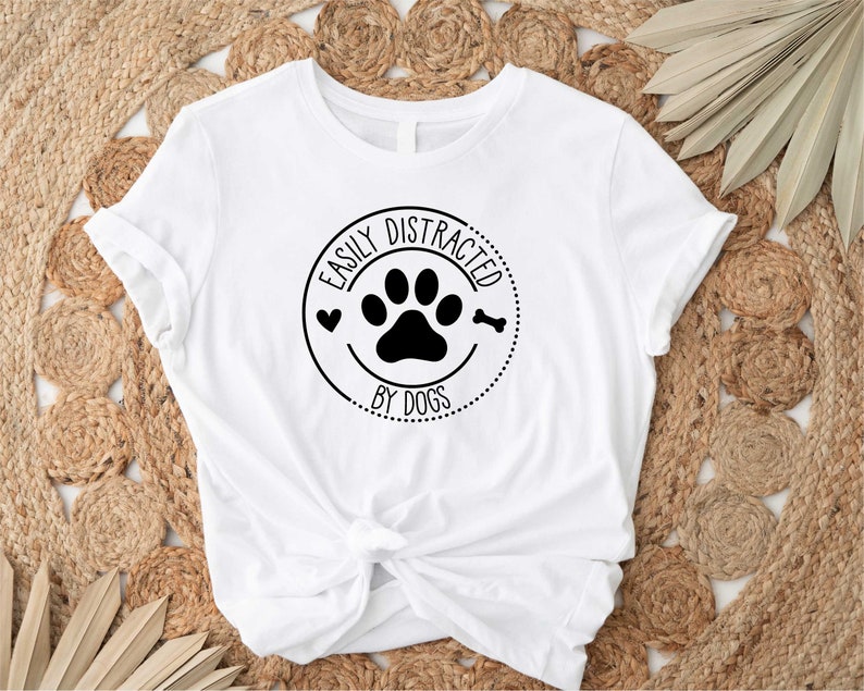 May include: White t-shirt with a black circle graphic that says "Easily Distracted by Dogs" with a paw print and bone inside the circle.