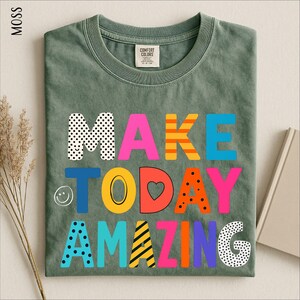 A green t-shirt with the text "MAKE TODAY AMAZING" printed on it, along with various colorful and playful lettering designs.