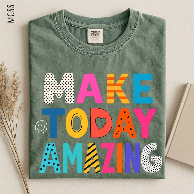 A green t-shirt with the text "MAKE TODAY AMAZING" printed on it, along with various colorful and playful lettering designs.