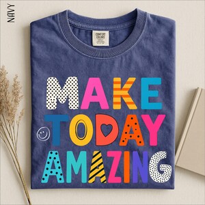 A navy blue t-shirt with the text "MAKE TODAY AMAZING" printed on it in a colorful, playful font.