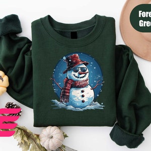 a green shirt with a snowman wearing a hat and scarf