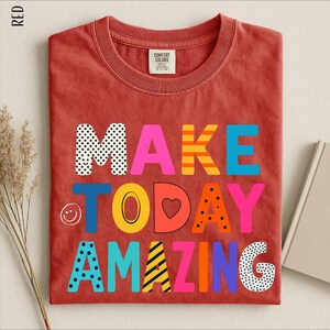 A red t-shirt with the text "MAKE TODAY AMAZING" printed on it, along with various colorful and playful lettering designs.