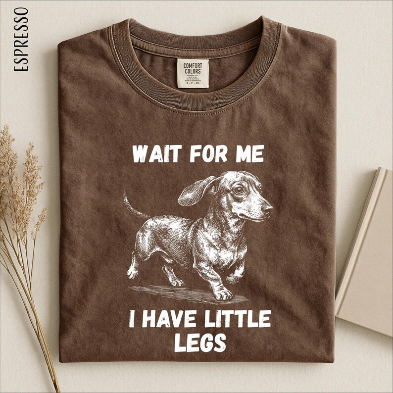 a brown t-shirt with a graphic of a dog and the text "WAIT FOR ME I HAVE LITTLE LEGS" printed on it.