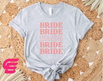 May include: A gray t-shirt with the word "BRIDE" repeated five times in a stacked, retro-style font in a light pink color.