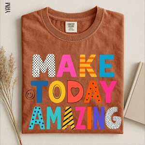 A brown t-shirt with the text "MAKE TODAY AMAZING" printed on it, along with various colorful and playful lettering designs.