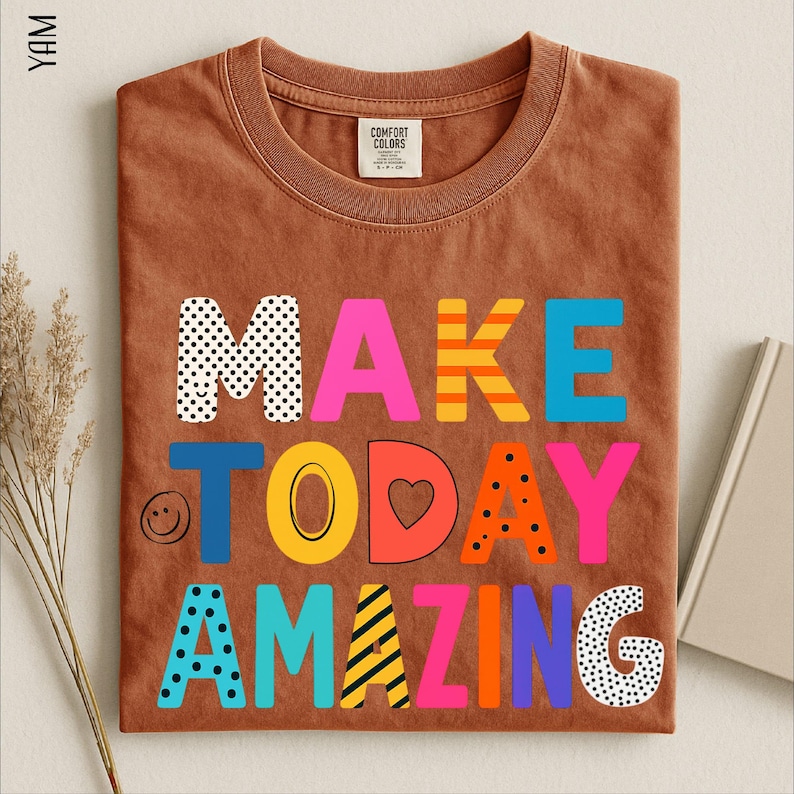 A brown t-shirt with the text "MAKE TODAY AMAZING" printed on it, along with various colorful and playful lettering designs.