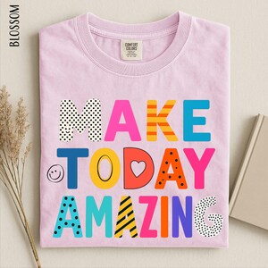 A pink t-shirt with the text "MAKE TODAY AMAZING" printed on it, along with various colorful and playful lettering designs.